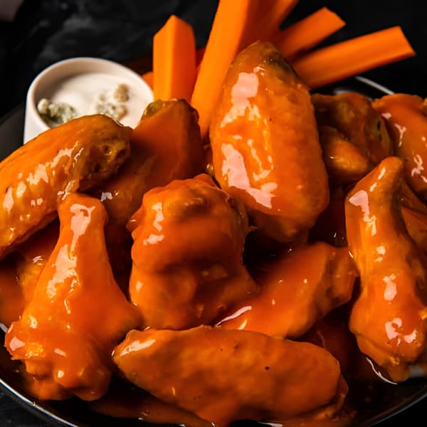 Close-up of Saoco's buffalo wings coated in orange sauce, with carrot sticks and ranch dip.
