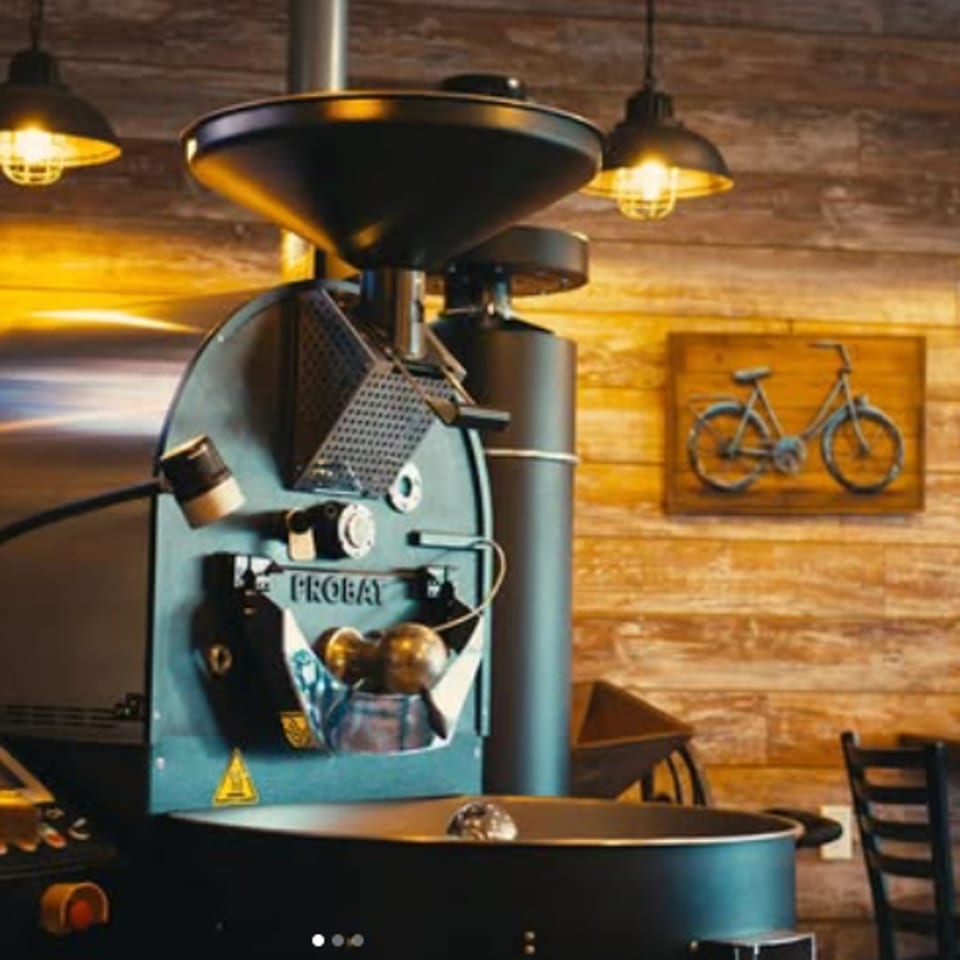Large coffee roasting machine with a wooden wall background and industrial pendant lights.