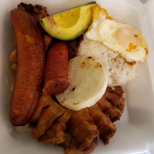 A Colombian platter with fried plantain, sausage, avocado, rice, fried egg, and chicharron.