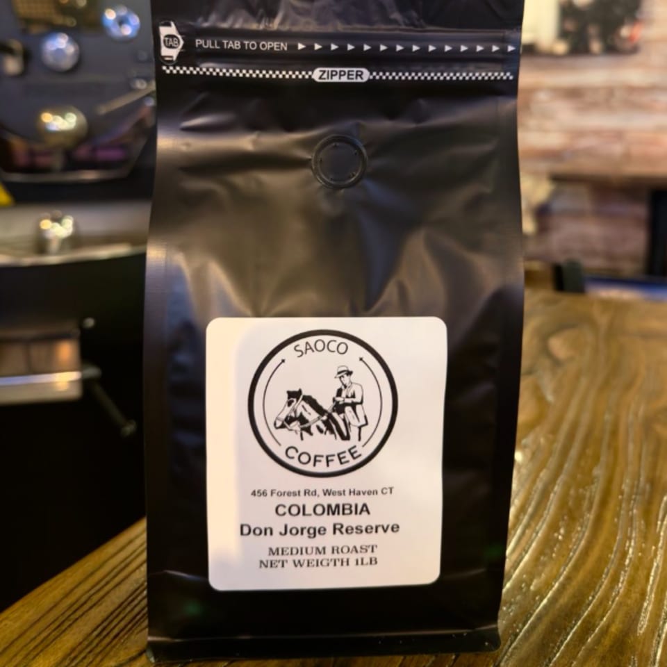 A black bag of Saoco Colombian Don Jorge Reserve medium roast coffee on a wooden surface.
