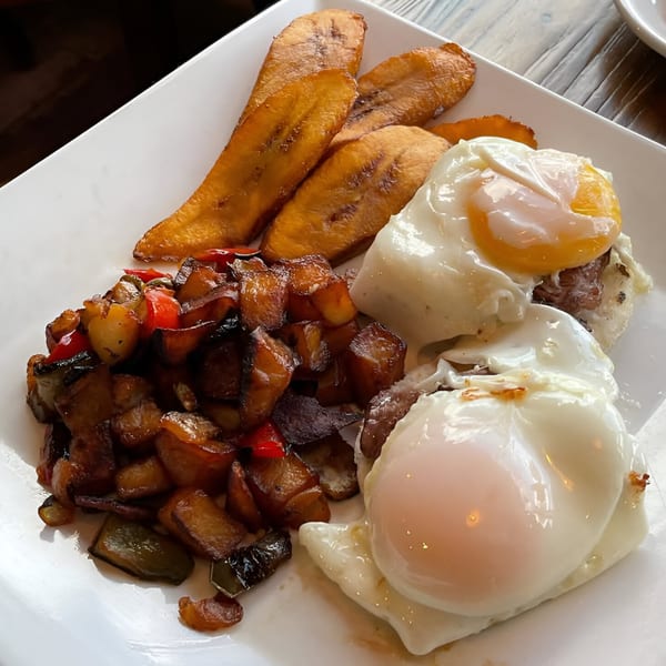 Colombian breakfast with fried plantains, diced potatoes and peppers, and two fried eggs on a white plate.