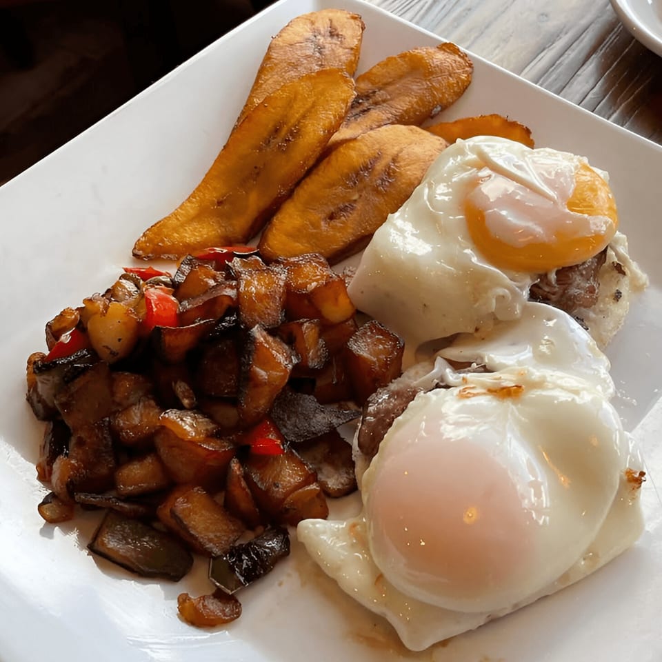 Colombian breakfast with fried plantains, diced potatoes and peppers, and two fried eggs on a white plate.
